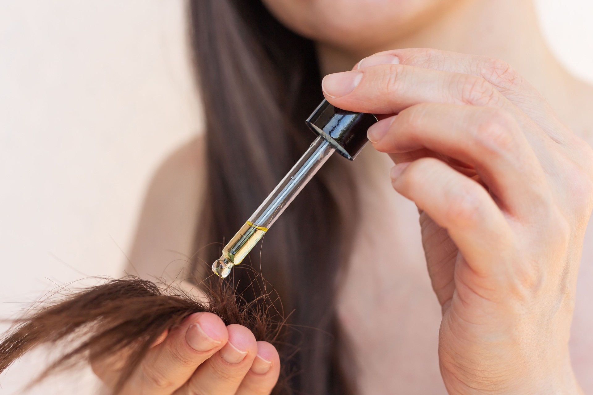 Young pretty woman applying natural oil to her hair against breakage and split ends